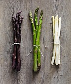 Purple, green and white asparagus stalks on a wooden surface