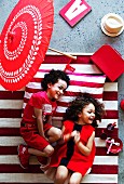 Laughing children dressed in red on red and white striped rug