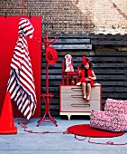 Bright red home accessories and furniture with little girl in red dress sitting on chest of drawers