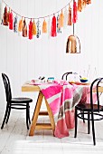 Cheerful tablecloth on dining table below copper pendant lamp and garland of shiny paper tassels