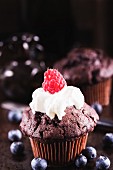 A chocolate cupcake with cream and a raspberry