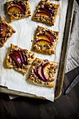 Puff pastry squares with red plum crumble on a baking sheet