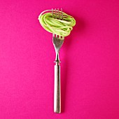 A fork with green pasta against a bright pink background