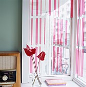 Vintage-Radio und Glasvase mit Flamingoblumen vor Fenster mit Streifenvorhang