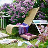Wickerwork lounger in front of flowering lilac bush