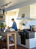 Woman in old, Swedish kitchen with large chimney breast over masonry range