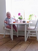 Baby sitzt auf Kinderstuhl am Tisch und isst Törtchen