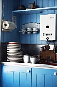 Detail of kitchen sink with stacked plates against blue-painted wooden wall
