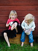 Mädchen mit Töpfen in der Hand sitzen und spielen vor Holzhauswand