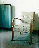 Biedermeier chair with torn upholstery and vintage radiator against wall