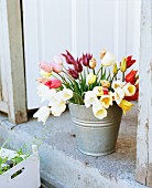 Colourful bouquet of tulips in zinc bucket on stone step of open exterior door