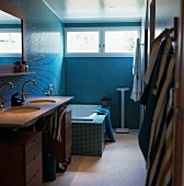 Bathroom with washstand and fitted bathtub against wall with blue mosaic tiles and transom windows