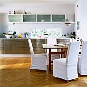 Fitted kitchen with stainless steel fronts and chairs with loose covers in dining area