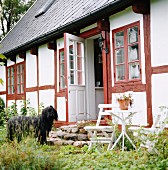 Hund vor altem, ländlichem Fachwerkhaus mit rot gestrichenen Fensterrahmen und Holzbalken