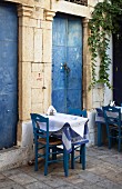 Gartentische in griechischem Terrassenlokal vor antiker Fassade mit verblichenen, blauen Metalltüren