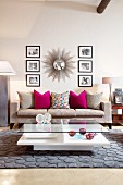 Sunburst mirror and black and white photographs above grey couch; crystal and glass ornaments on coffee table