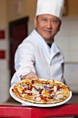Mature chef holding fresh pizza on plate, portrait