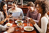 Friends at restaurant texting and showing photos using cell phones
