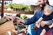 Familie mit kleinem Kind kauft Gemüse auf Markt