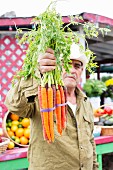 A farmer holding a bunch of carrots in assorted colours