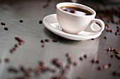 A cup of coffee surrounded by coffee beans