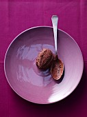 A quenelle of chocolate mousse on a purple plate with a spoon