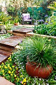 Kleiner terrassierter Garten mit gemütlichem Sitzplatz und grossem Tontopf mit Ziergras im Blumenbeet