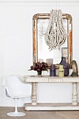 White tulip chair next to antique console table and hand-crafted pendant lamp in front of flyblown mirror