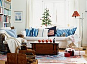 Pomegranates on wooden trunk in front of white sofa with blue and white striped scatter cushions below window in living room decorated for Christmas