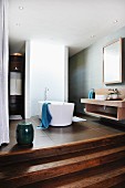 Free-standing bathtub in front of curved partition in open-plan, designer bathroom with wide wooden steps