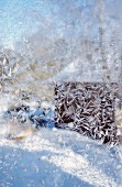 Blick durch vereiste Fensterscheibe auf Holzhäuschen im Schnee