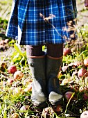 Girl wearing kilt & wellingtons standing amongst windfall apples