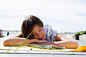 Bäuchlings auf Holzsteg liegende junge Frau, eingeschlafen beim Sonnenbaden