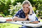 Frau lächelnd über provisorischen Handwerkertisch im Garten gebeugt