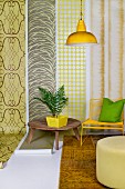 Holztisch mit Zimmerpflanze, gelber Stuhl und Pouf vor Tapetenbahnen