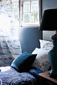 Blue-patterned pillows and blanket on bed below lattice window with curtain