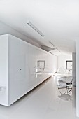 Long row of glossy, white wardrobes and 50s, tubular steel designer armchair on reflective white floor