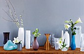 Unterschiedliche Vasen in Form und Stil kunstvoll mit Lilien arrangiert und vor grauer Wand in Szene gesetzt