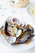 The remains of clams and mussels on a porcelain plate, with wine glasses and a bread basket