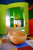 Walls and ceiling in bold shades of green and red; free-standing, oval bathtub on floor with large, square tiles in various colours