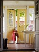 Mädchen mit Teddybär schaut aus geöffneter Haustür