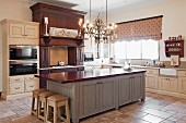 Nostalgic country-house kitchen with lit chandelier above island counter with dark, solid wood worksurface