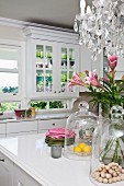 Elegante Landhausküche mit Blick in die Landschaft; im Vordergrund ein Sommerblumenstrauss unter einem Kristallleuchter