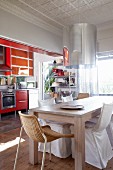 Essbereich mit modernem Holztisch und verschiedenen Stühlen vor Küche mit roten Fronten