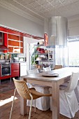 Dining area with modern wooden table and various chairs in front of kitchen with red units