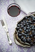 Red grapes, a glass of red wine, a napkin and silver cutlery
