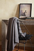 Table made from massive wooden slabs and grey woollen blanket hanging over delicate metal chair