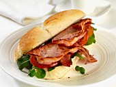 A bread roll filled with bacon, tomatoes, rocket and watercress