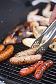 Barbecued sausages being turned with barbecue tongs