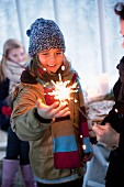Girl wearing winter clothing looking at sparkler